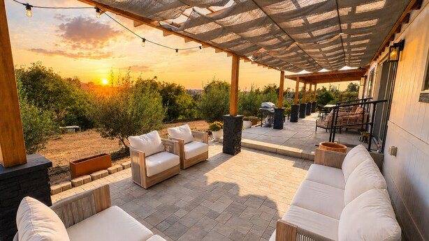 Eine Terrass mit überdachter Sitzgruppe, einem Grill und Blick auf den Sonnenuntergang.