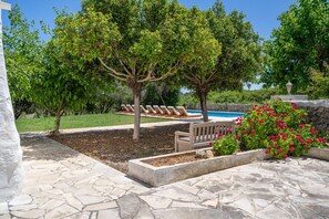 Un área de piscina con sillones de descanso, un banco de madera y un parterre floral.