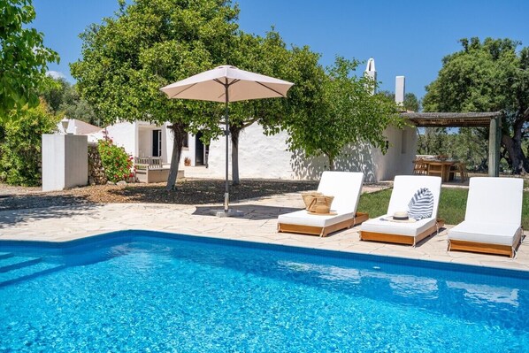 Una piscina con sillones de descanso y una sombrilla.