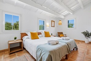 Un dormitorio con dos camas, una mesita de noche de madera, una silla de mimbre y una planta en maceta.