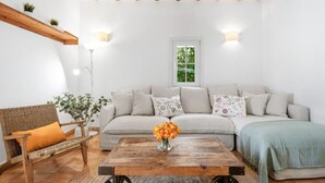Een woonkamer met een bank, een houten salontafel, een rieten fauteuil en een raam met uitzicht op groen.