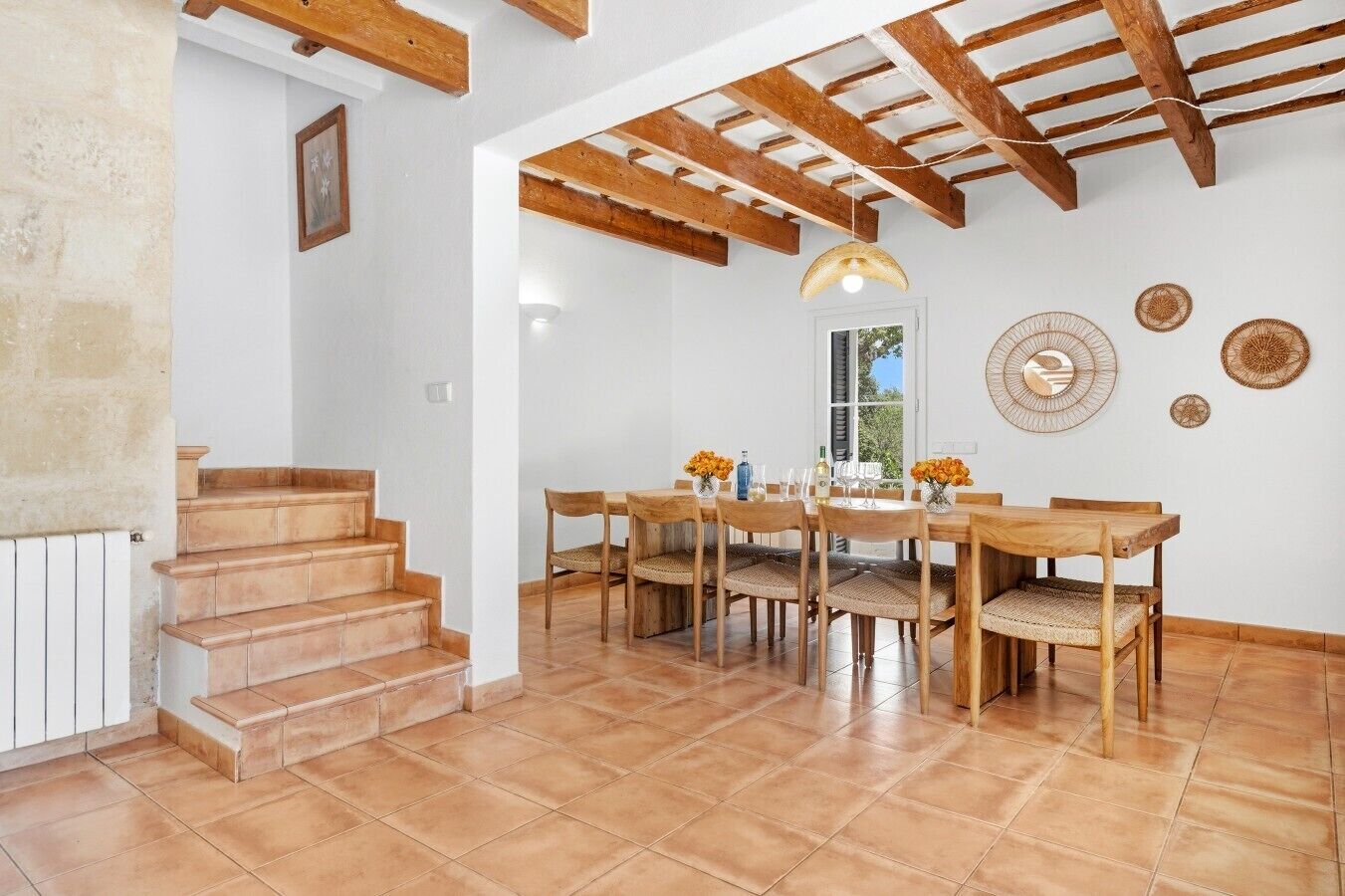 Un espace repas avec une table et des chaises en bois, un escalier et un plafond avec des poutres apparentes.