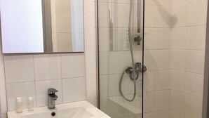 Ett badrum med en dusch som är avskärmad med glasväggar, ett vitt handfat med två flaskor och en spegel ovanför handfatet.