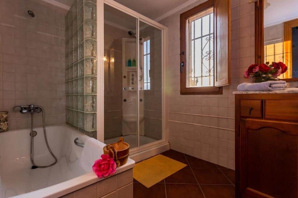 Un baño con bañera, ducha con mampara de cristal, tocador con espejo y ventana.