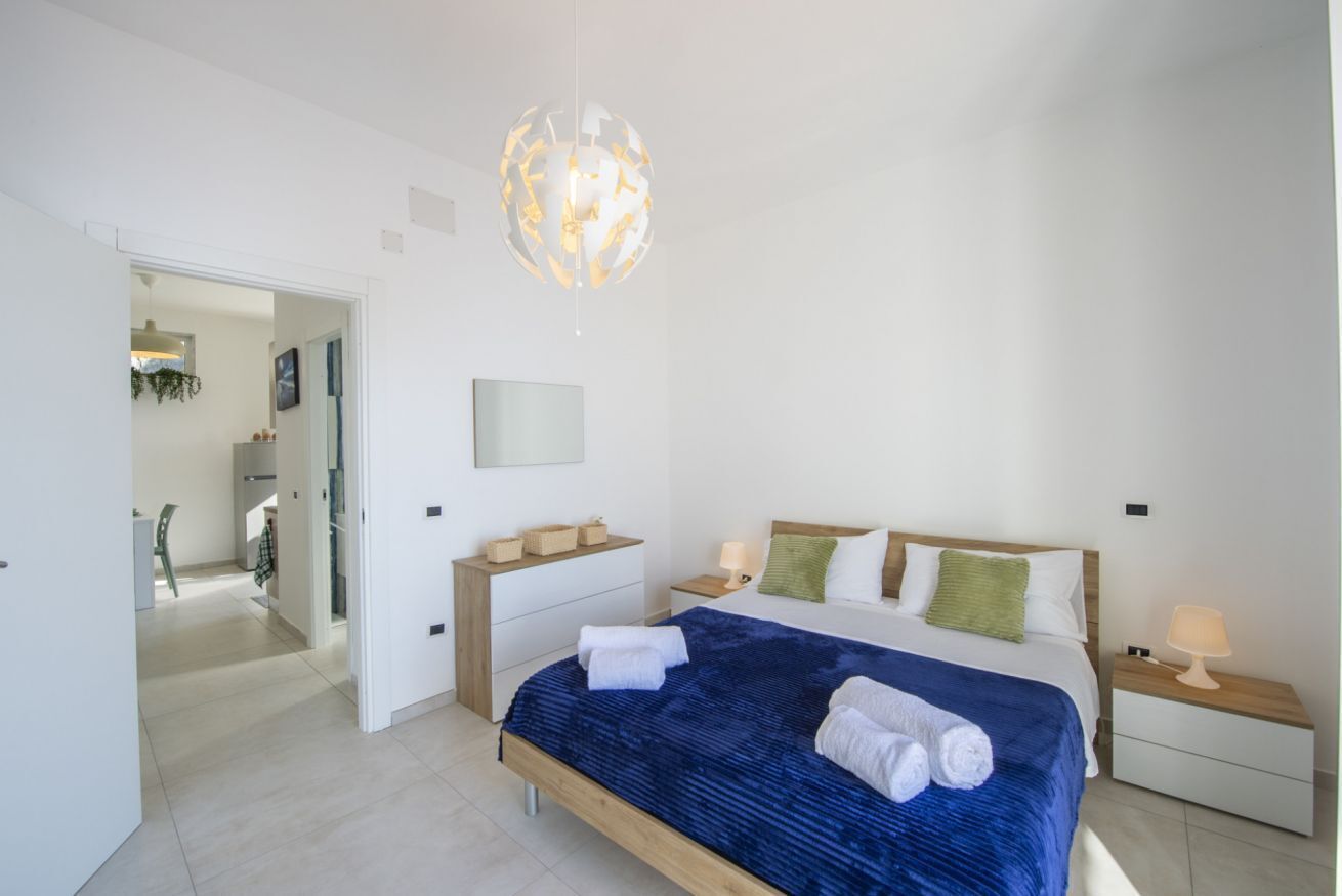 Ein modernes Schlafzimmer mit einem großen Bett, Nachttischen, einer Hängeleuchte und Blick in einen weiteren Raum.