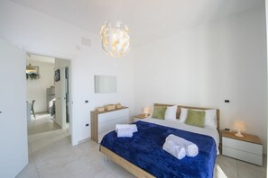 A modern bedroom with a large bed, bedside tables, a hanging light fixture, and a view into another room. - VivimiHome-Casa Angelina (Conca dei Marini)