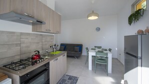 Et moderne køkken med gasblus, ovn og emfang. Der er et spiseområde med et bord og stole, samt en grå sofa.