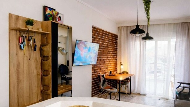 Ein modernes Wohnzimmer mit einem weißen Sofa, einem Holzschrank mit Werkzeugen, einem Fernseher an der Wand und einer Ziegelwand als Blickfang.