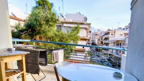 Ein Balkon mit rundem Tisch und Stühlen, einem Grill und Blick auf eine Wohngegend mit Häusern und Bäumen.