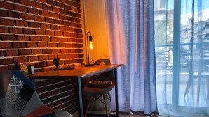 Ein gemütliches Zimmer mit Backsteinwand, einem Holztisch, einem gepolsterten Stuhl und einem großen Fenster mit durchsichtigen Vorhängen.