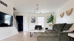 A modern living room with a sectional sofa, a flat-screen TV, a coffee table, and a staircase leading to another level. - Shoreham Luxe - Vibrant 4BR\2.5BA with Waterfront (Evansville)