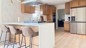 A modern kitchen with a central island, bar stools, wooden cabinets, stainless steel appliances, and pendant lighting. - Shoreham Luxe - Vibrant 4BR\2.5BA with Waterfront (Evansville)