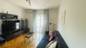 Ein modernes Wohnzimmer mit einem schwarzen Sofa, Holzdielen im Fischgrätmuster und einem Flachbildfernseher.