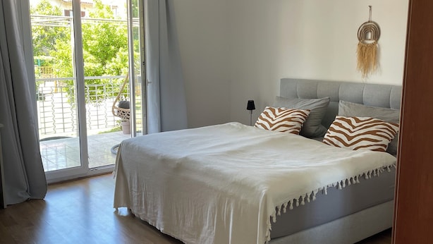 Ein Schlafzimmer mit Bett, Deckenventilator, Blick durch eine Schiebetür und Wandleuchte.