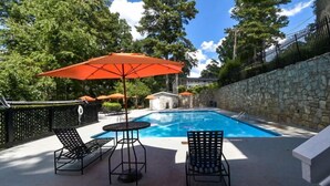 Une piscine entourée d’un mur de pierre et d’arbres, avec des chaises longues et des parasols.