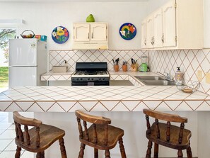 A kitchen with a gas stove, white cabinets, a tiled backsplash, and wooden chairs. - Quiet Mexican-style Getaway With Spacious Patio (Puerto Peñasco)