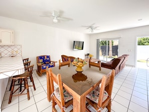 Uma sala de jantar com uma mesa e cadeiras de madeira, um ventilador de teto e uma televisão na parede.