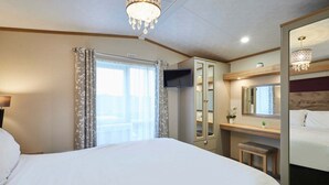 Quarto de hotel com uma cama grande, uma escrivaninha com espelho, um pequeno banco e um candelabro.