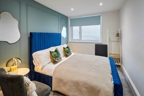 A bedroom with a large bed, a bedside table with a lamp, a chair, a window with a view, and a wardrobe. - Host and Stay The Seaview Lookout (Scarborough)