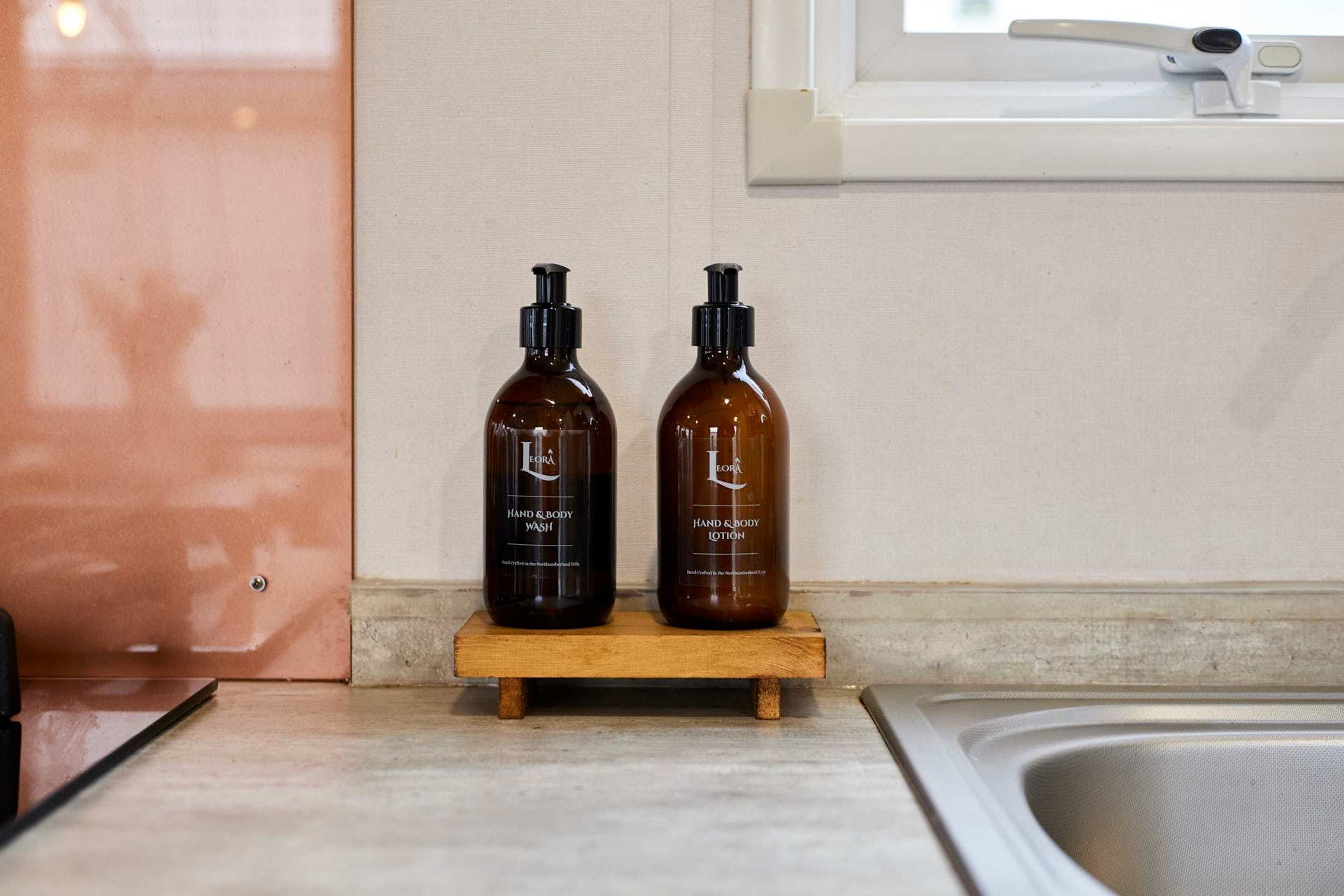 Two bottles of hand and body wash on a wooden shelf in a bathroom.