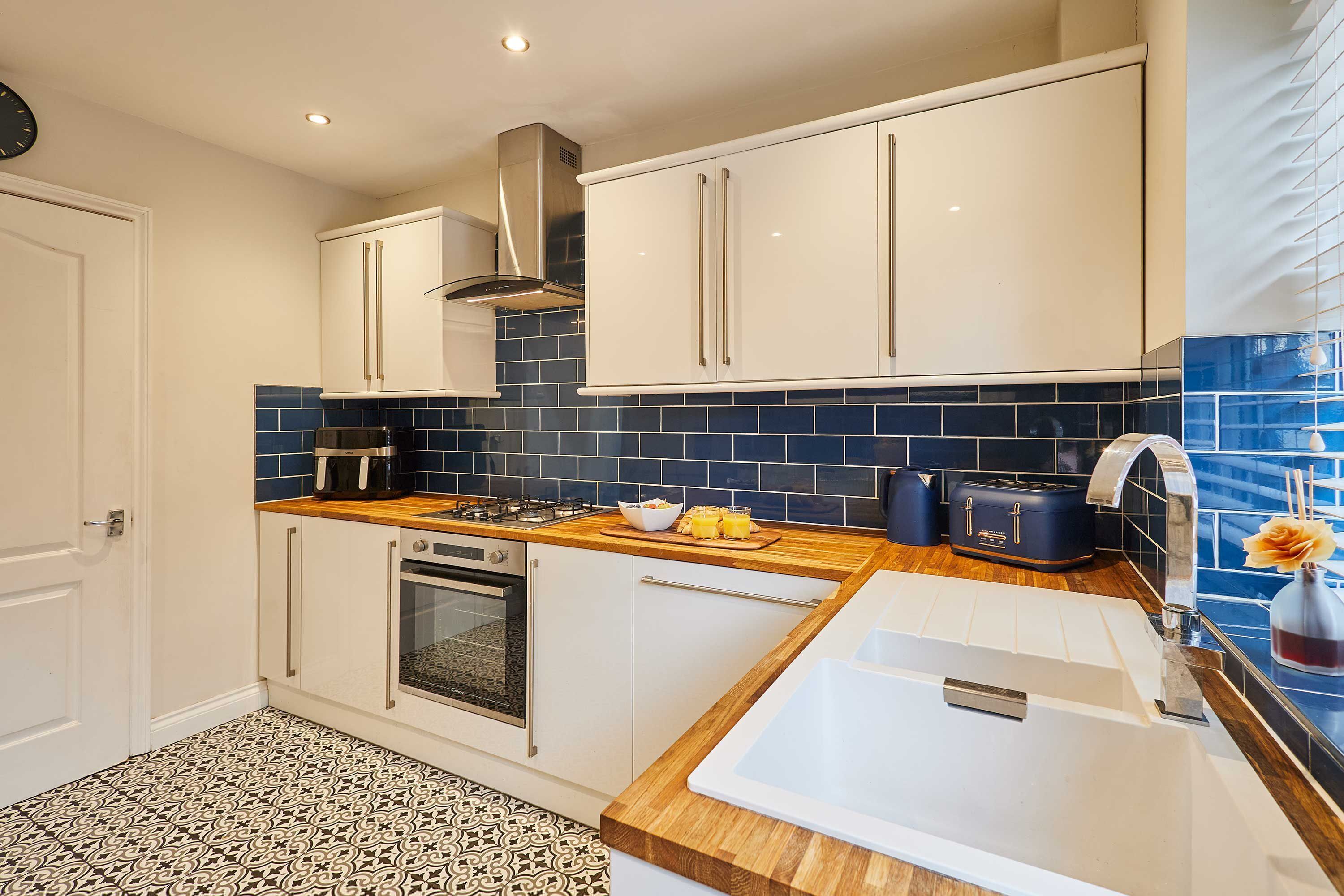 A modern kitchen with white cabinets, a stainless steel range hood, a built-in oven, and a wooden countertop.