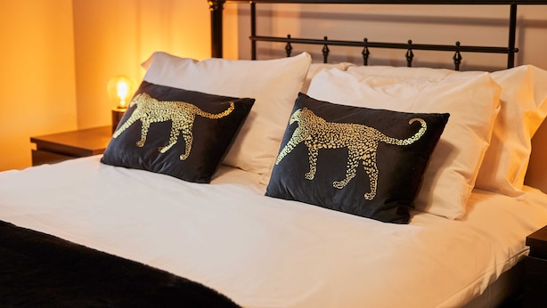 Un lit avec une literie blanche et deux oreillers noirs ornés d’un motif représentant un éléphant doré.