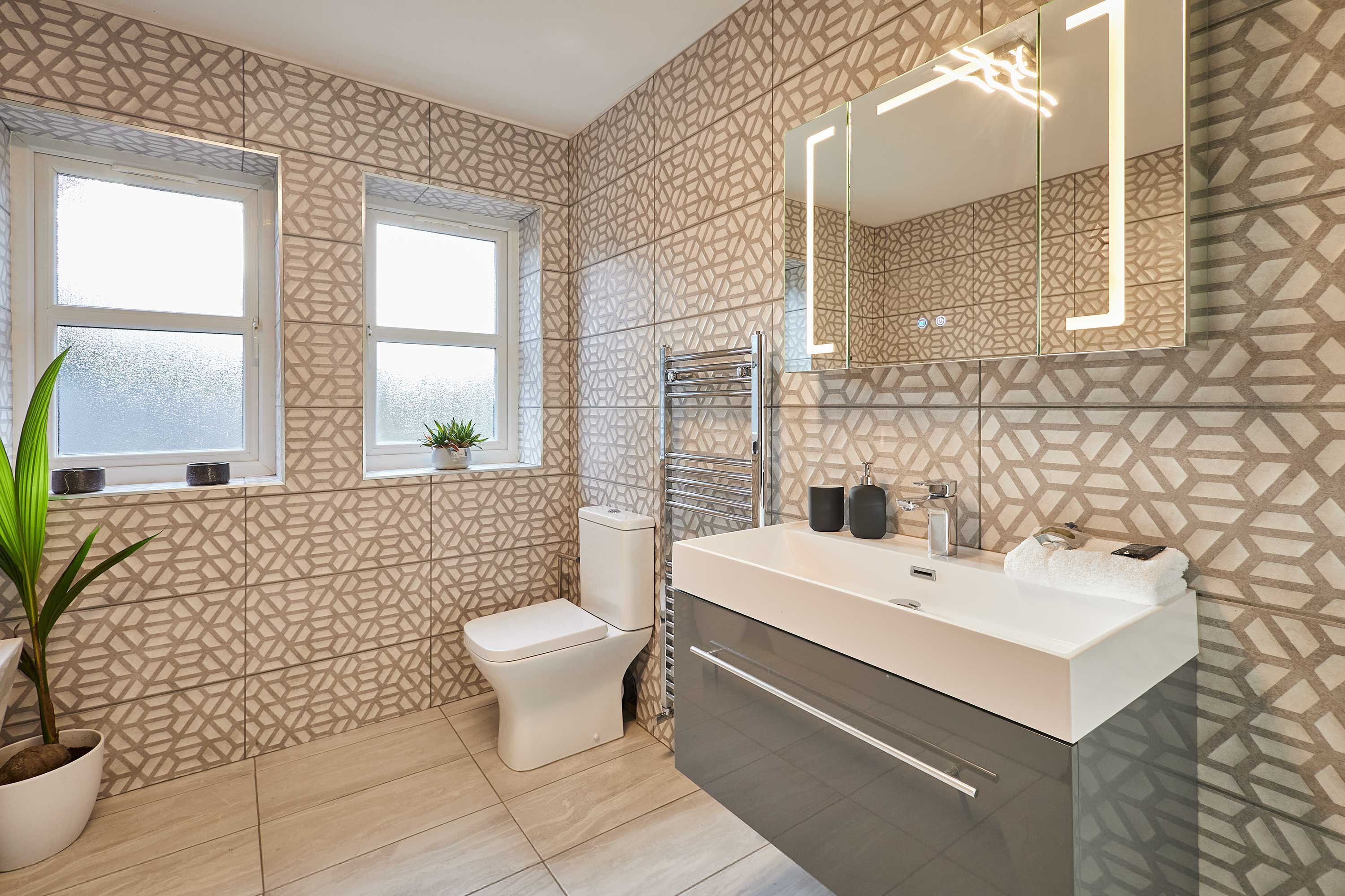 A modern bathroom with a geometric patterned wall, a toilet, a sink with a mirror, and a potted plant.