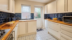 Une cuisine moderne avec des meubles blancs, un plan de travail en bois, un carrelage noir et blanc à motifs et une fenêtre avec des stores.