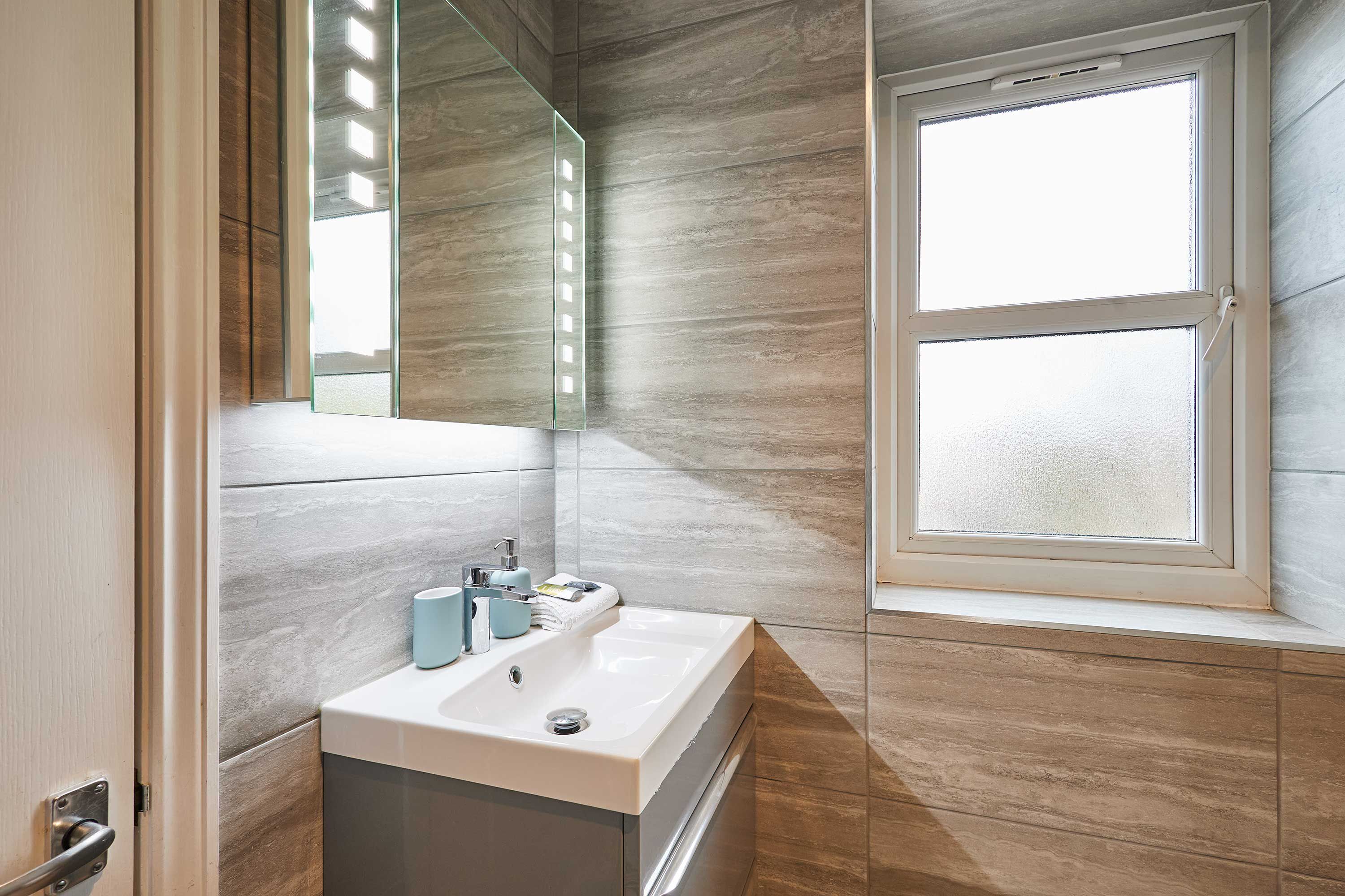 Une salle de bain moderne avec un lavabo blanc, un miroir et des carreaux de couleur claire.