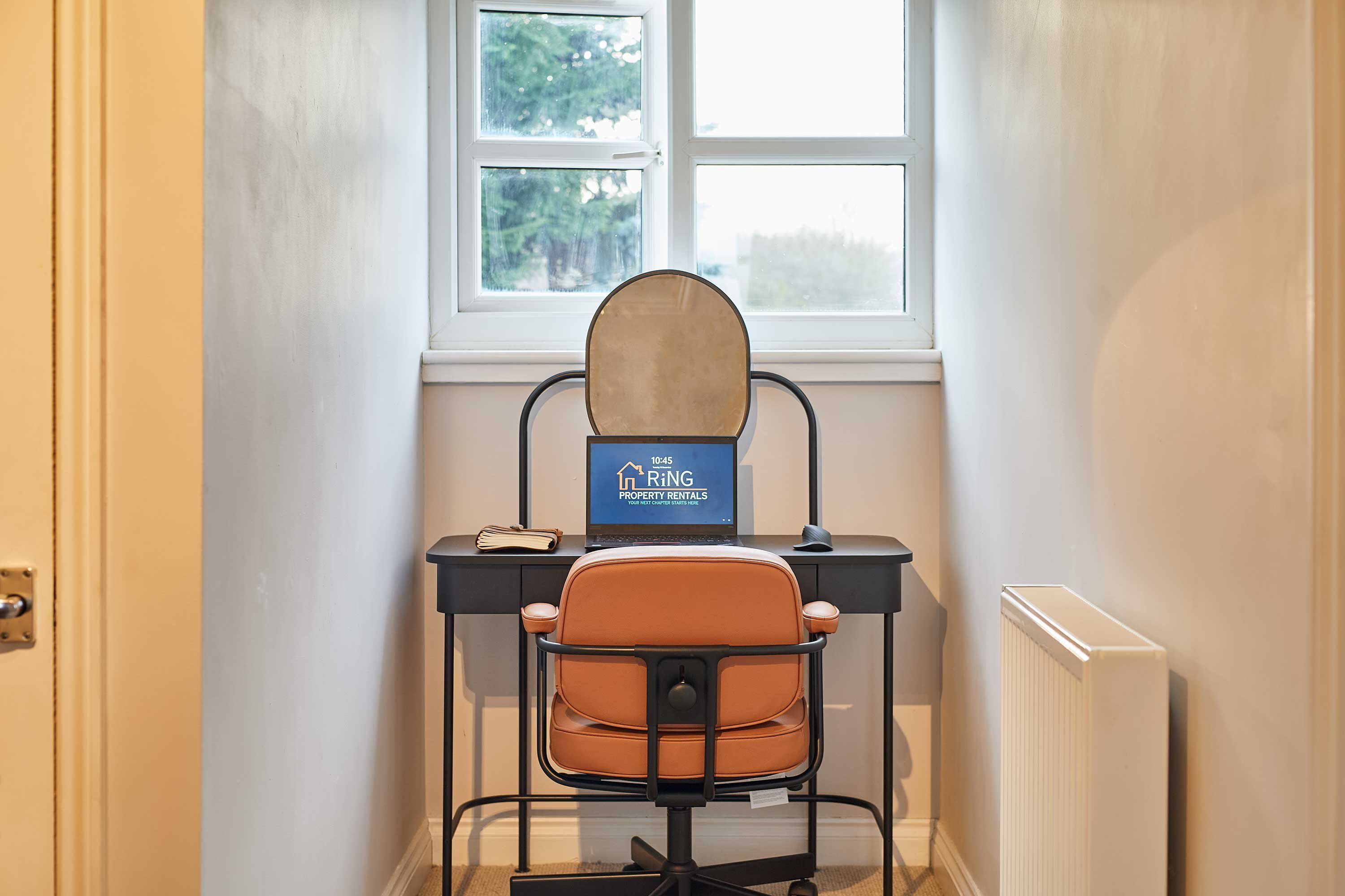 A small office space with a desk, a chair, a computer, and a window.