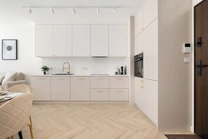 Une cuisine moderne avec des meubles blancs, un parquet en chevrons et un coin repas comprenant une table et des chaises blanches.