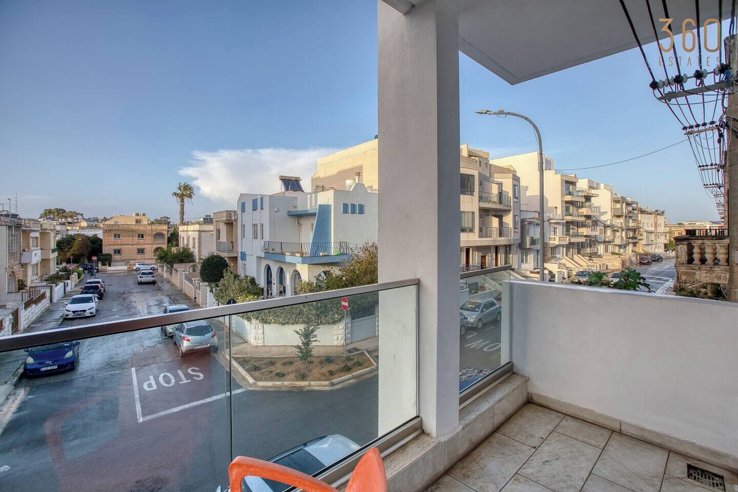 Un balcone con vista su una strada residenziale, un segnale di stop e cielo sereno.