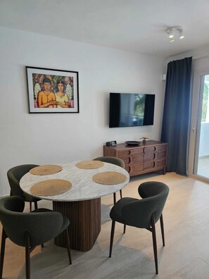 Zona pranzo moderna con un tavolo rotondo, quattro sedie, un mobiletto in legno e una televisione a schermo piatto appesa al muro.