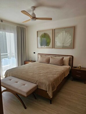 Una camera da letto con un letto, una panca, un comodino, una ventola a soffitto e due quadri appesi al muro.