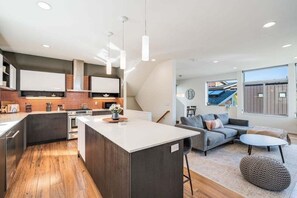 Une cuisine moderne dotée d’un îlot central, d’appareils électroménagers intégrés et de luminaires suspendus.