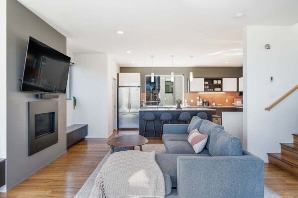 Un salon moderne avec un canapé gris, un téléviseur à écran plat fixé au mur et une petite table basse.