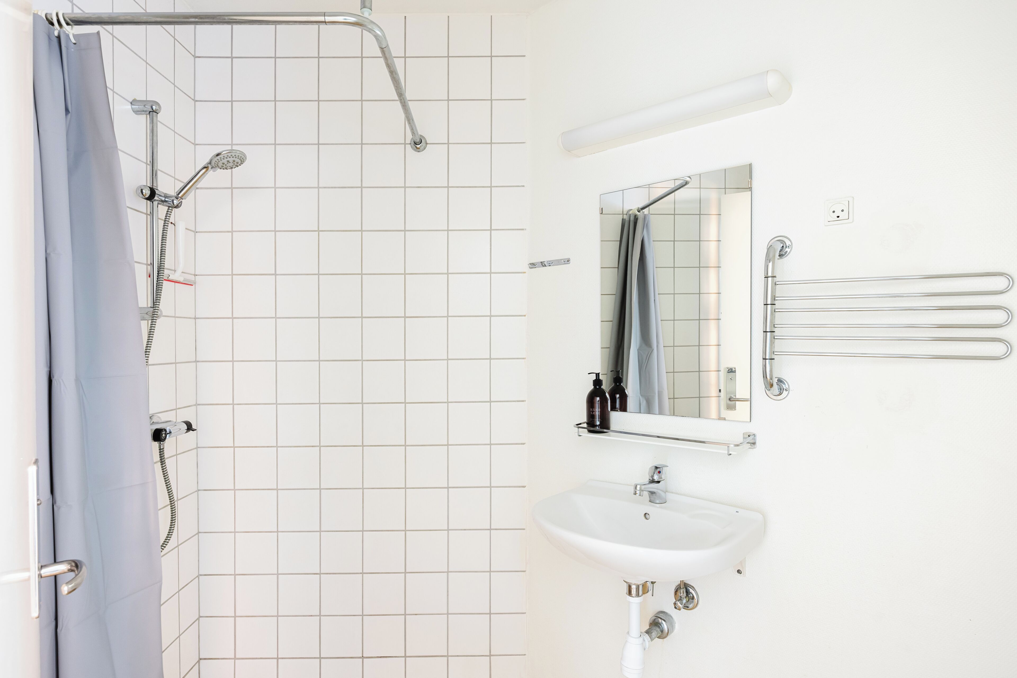 A bathroom with a shower, a sink, a mirror, and a towel rack.