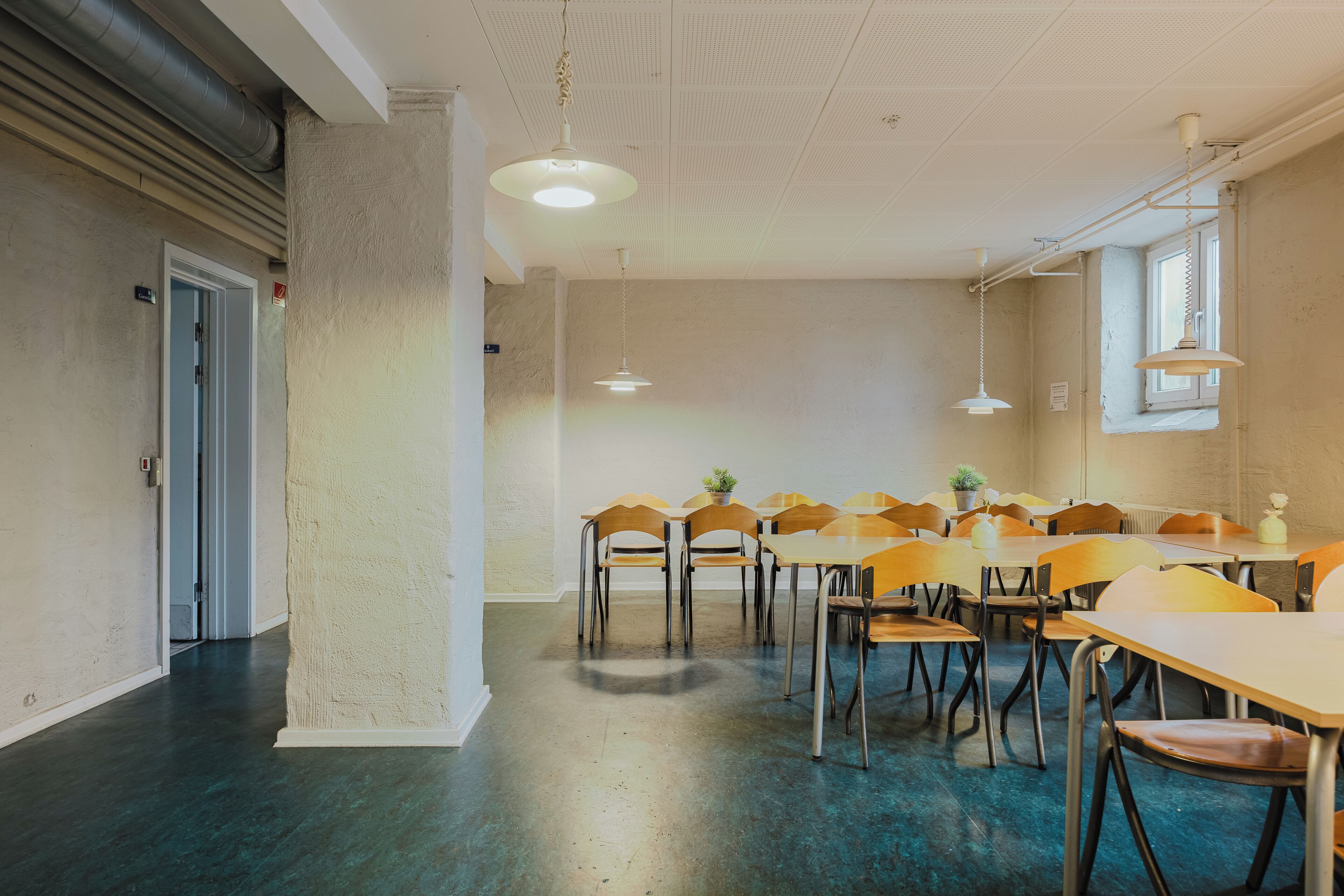 A conference room with a long table and chairs, a ceiling with a grid pattern, and a window with blinds.