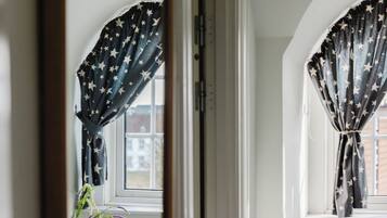 Una habitación con ventana, cortinas con estampado de estrellas, una puerta blanca y vista a un edificio exterior.