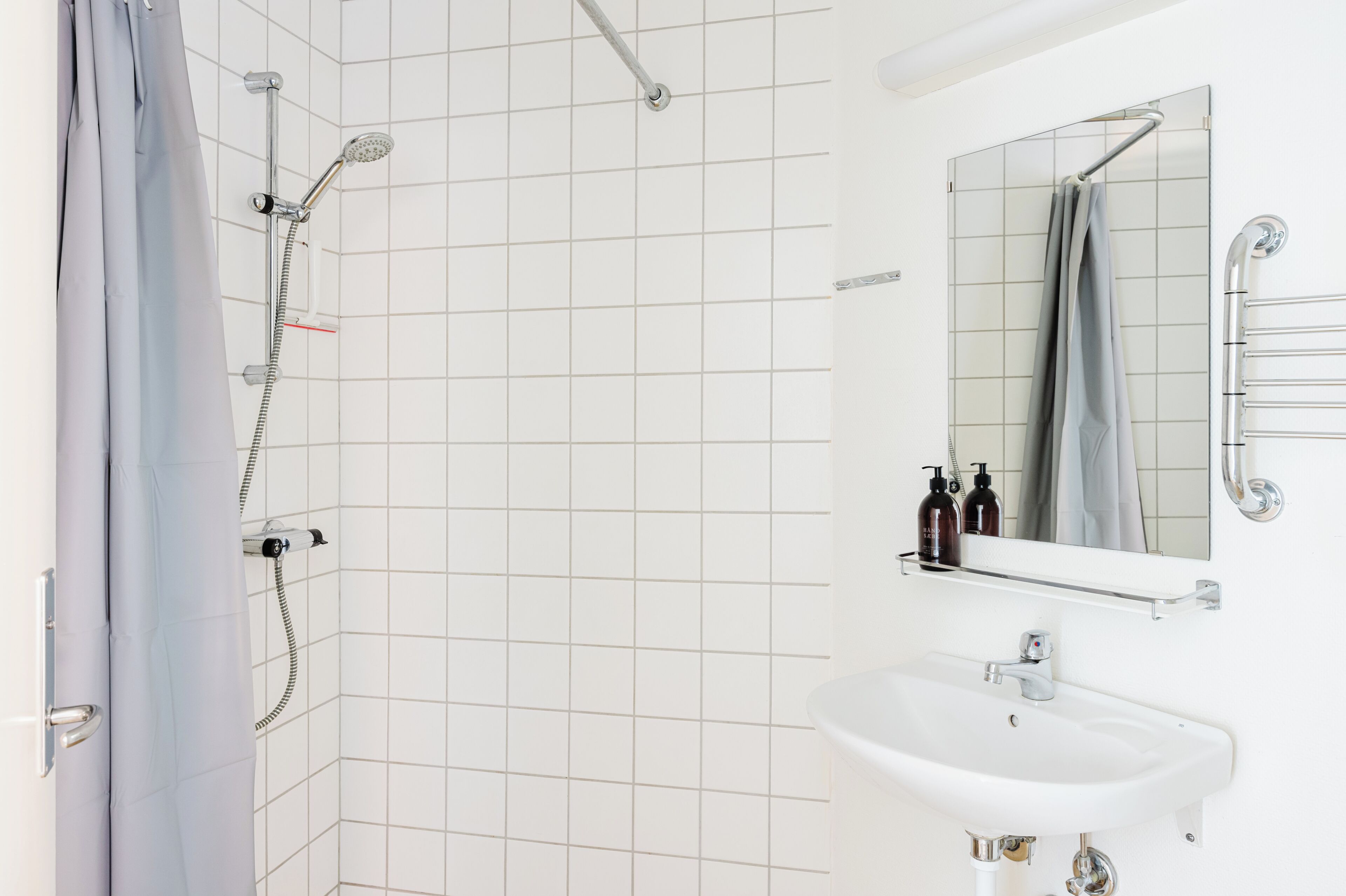 A bathroom with a shower, a sink, a mirror, and a towel rack.