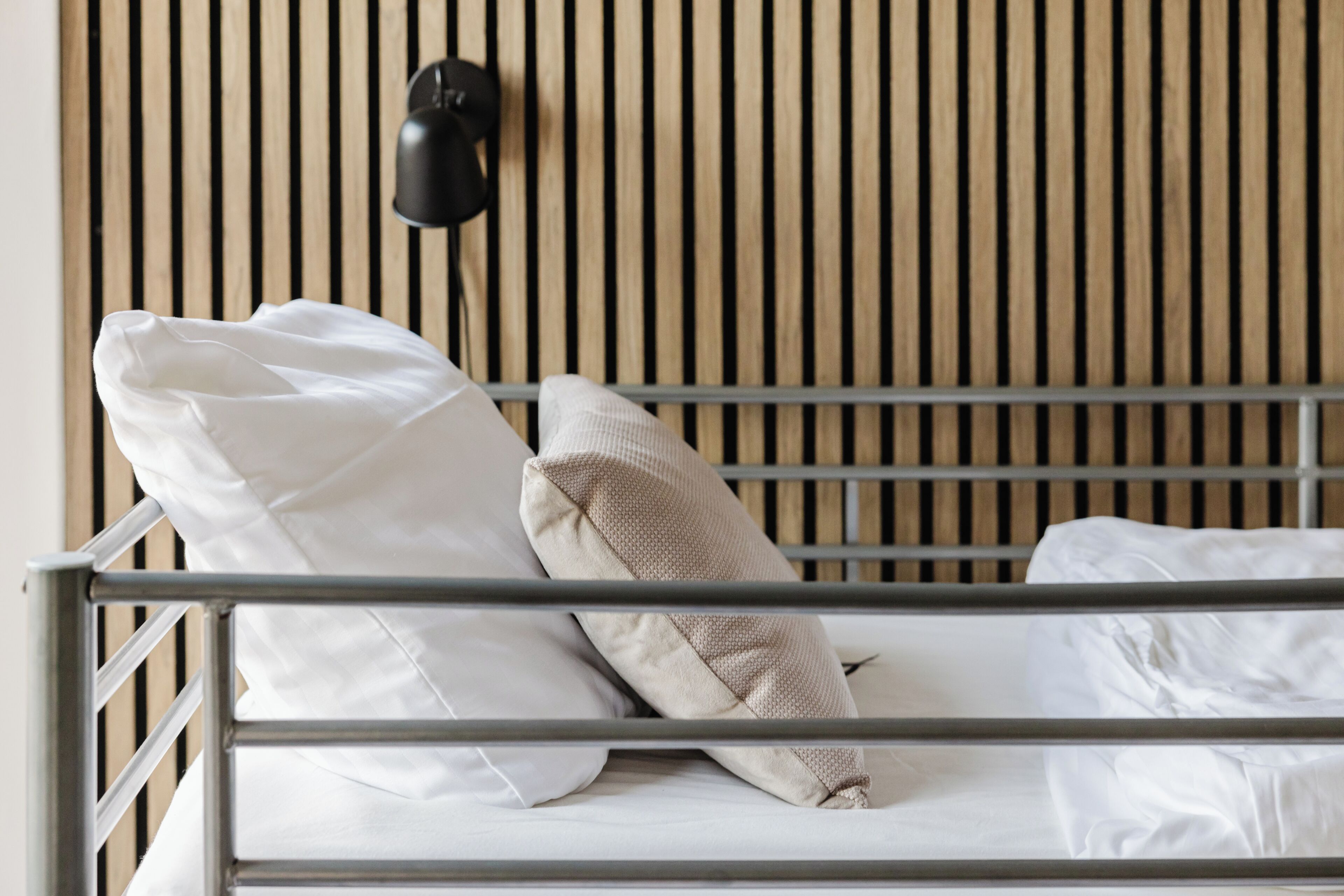 A bed with white bedding and a metal frame, a beige pillow, and a black wall-mounted lamp.