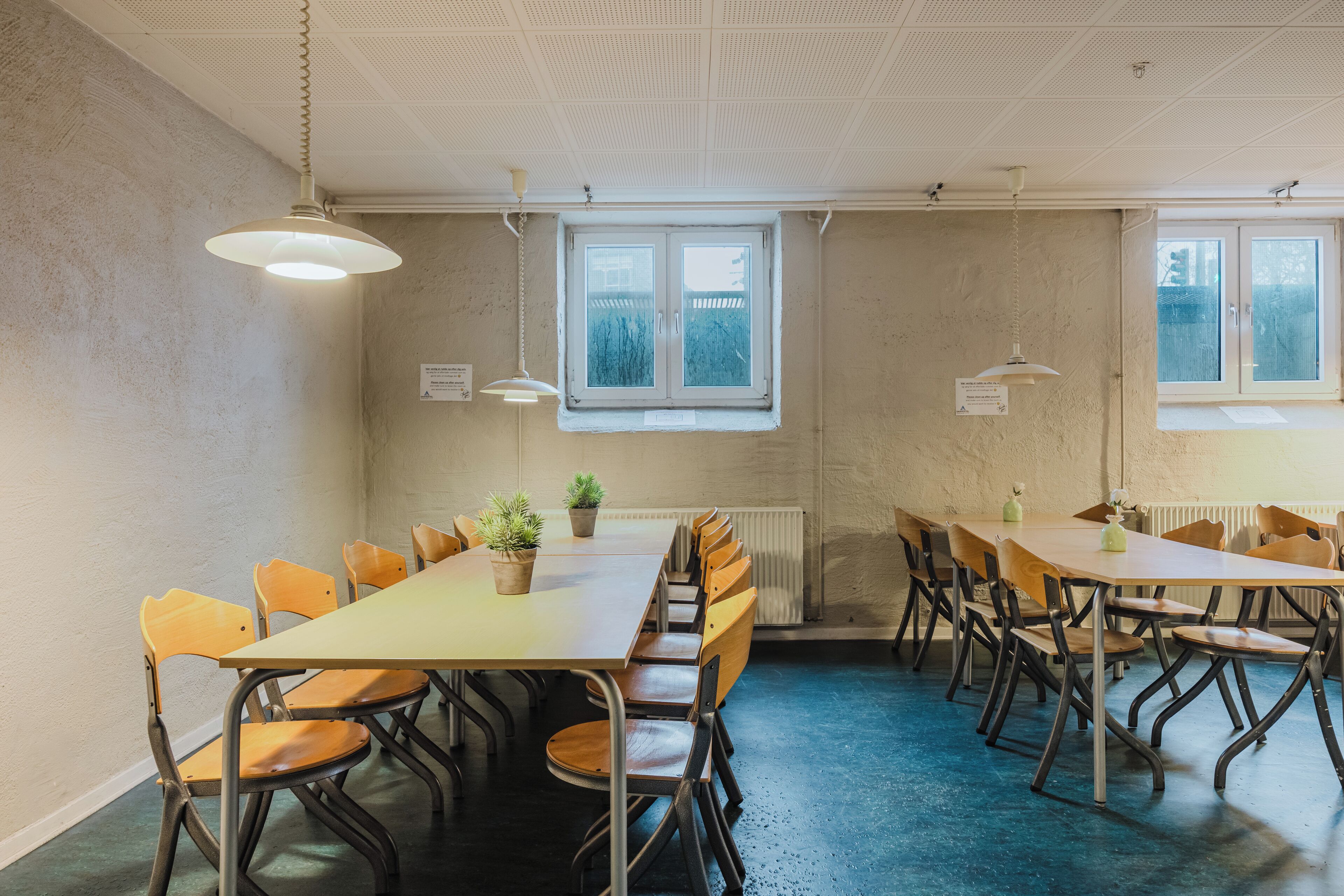 Une salle de conférence avec une longue table, des chaises, des plantes en pot et deux fenêtres équipées de stores.
