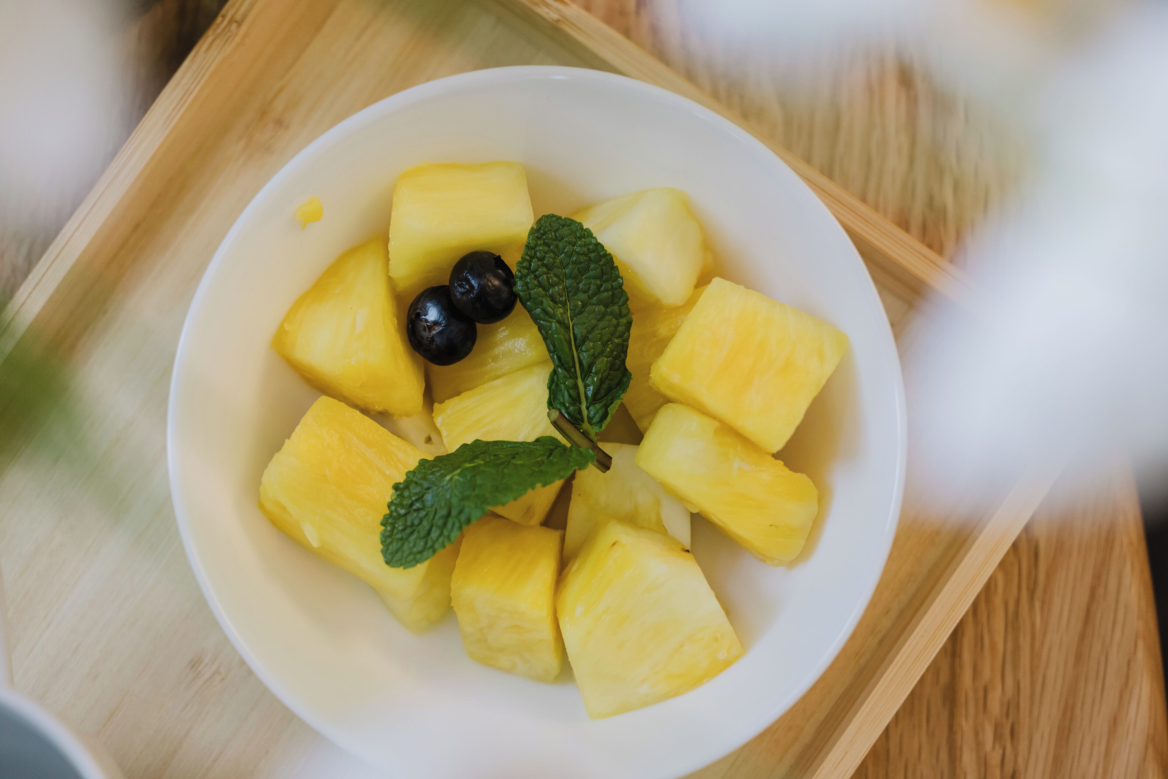 A bowl of pineapple chunks and black olives on a wooden tray.