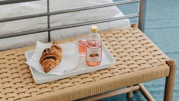 Una poltrona in vimini con un vassoio contenente un cornetto, un bicchiere di bevanda rosa e una bottiglia di limonata.