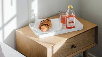 Una mesita de noche de madera con una bandeja blanca que sostiene un croissant y una botella de limonada.
