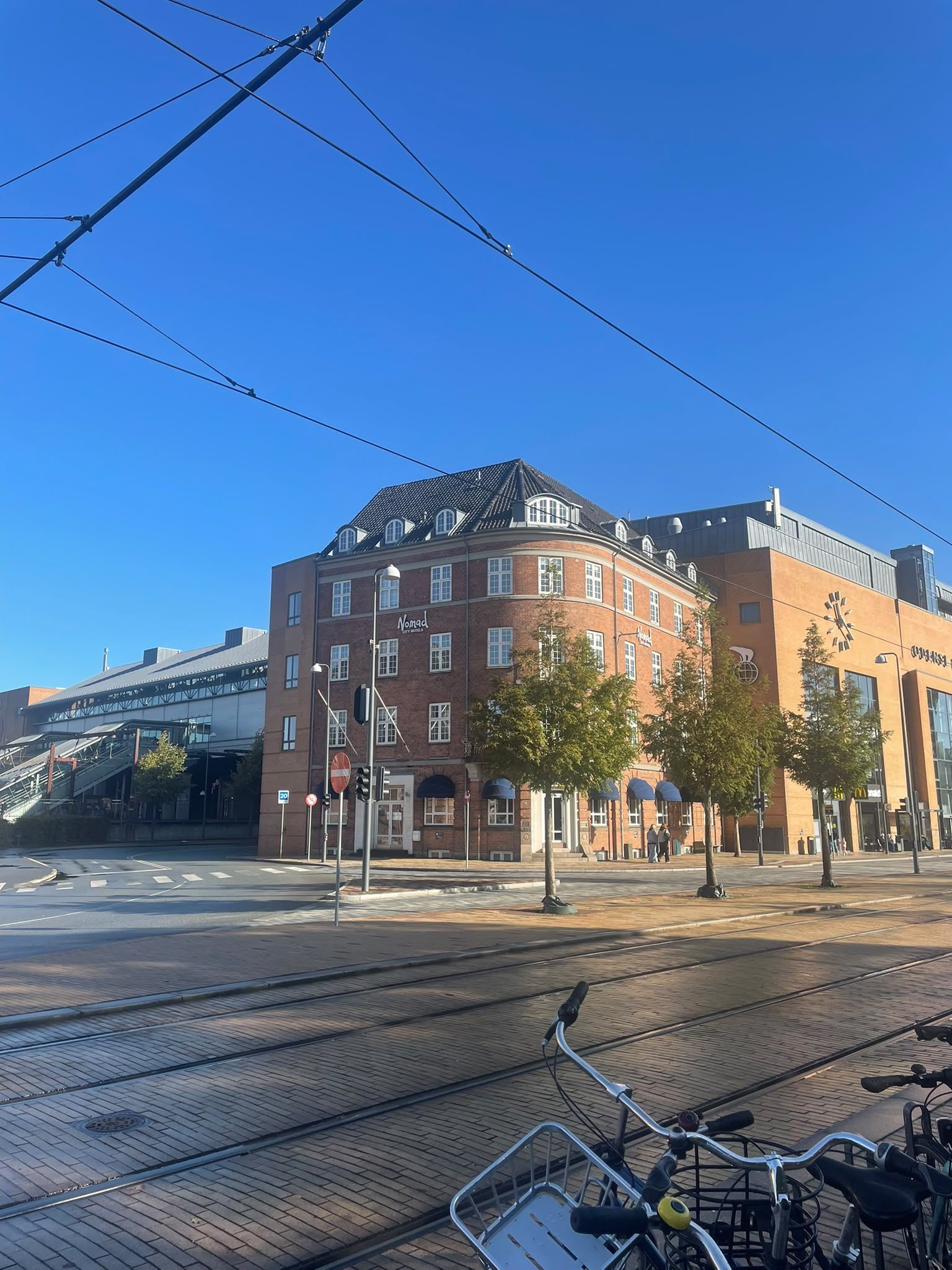 Un edificio con ingresso d'angolo, una linea tramviaria e un'area di parcheggio per biciclette.