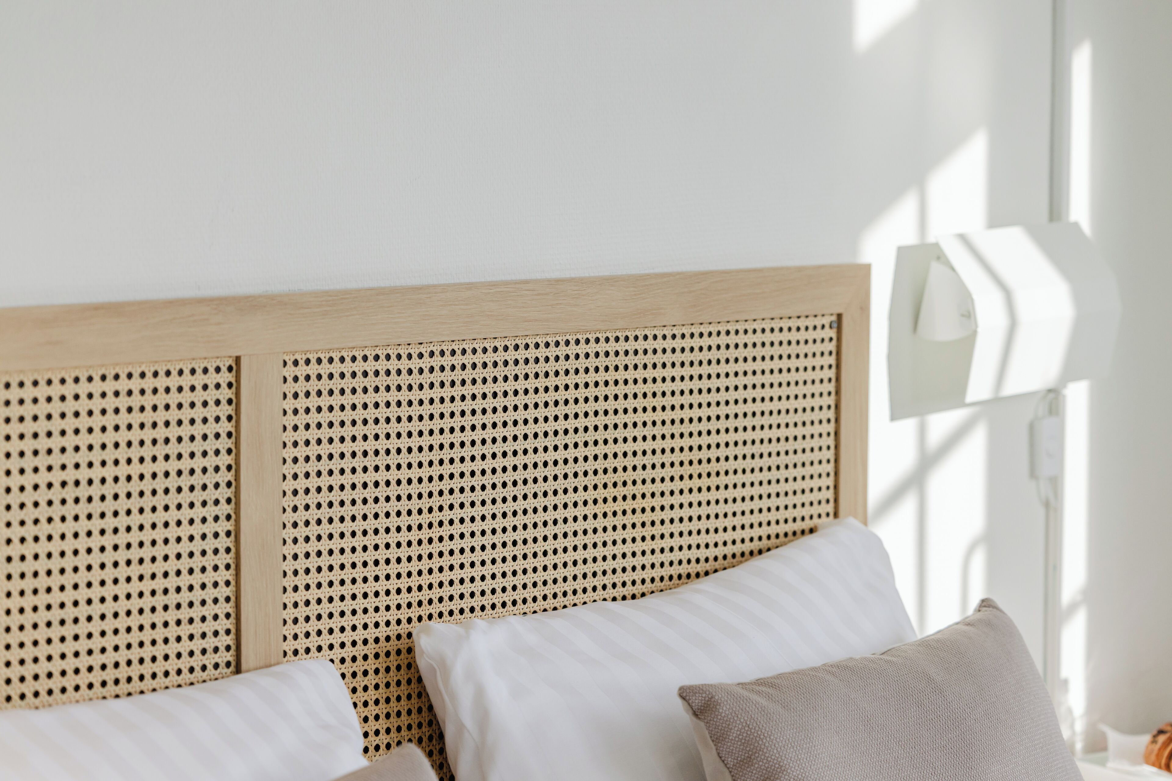 A bed with a wooden headboard, white bedding, and a white bedside lamp.