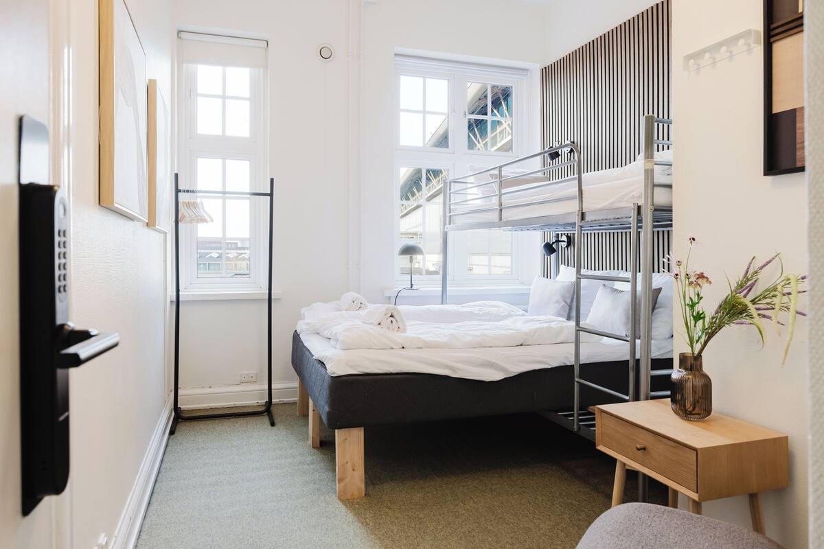 A room with bunk beds, a bedside table, a chair, a window, and a door.