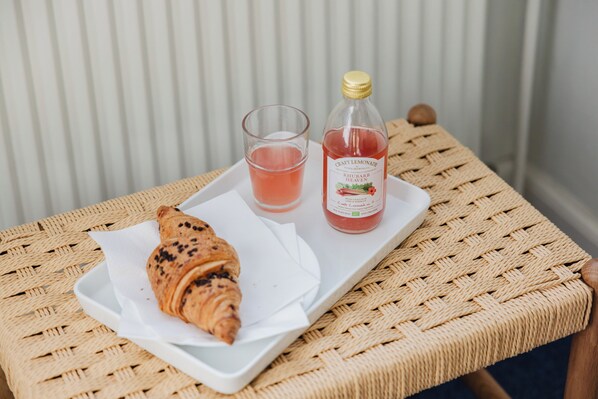 A wicker table with a croissant, a glass of pink drink, and a bottle of lemonade.