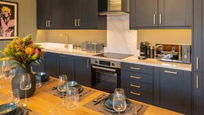 Une cuisine moderne avec des meubles de couleur sombre, un four encastré et un plan de travail sur lequel se trouvent une machine à café et un grille-pain.